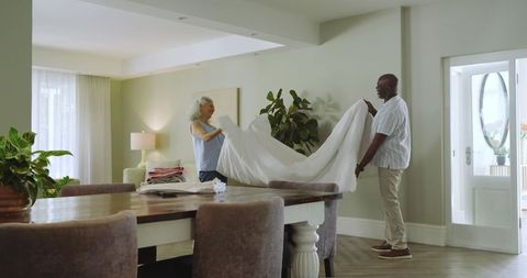 Senior couple folding sheet together in cozy home dining room