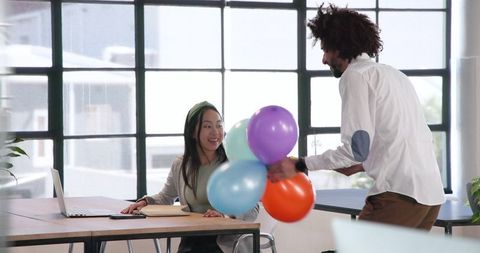 Joyful Office Scene: Man Bringing Balloons to Colleague