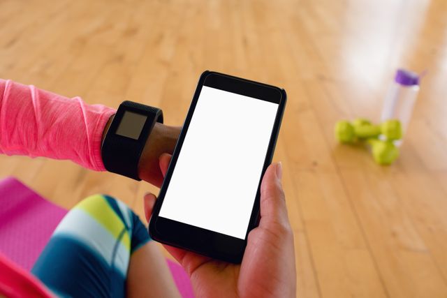 Woman holding mobile hone while using smartwatch in the gym