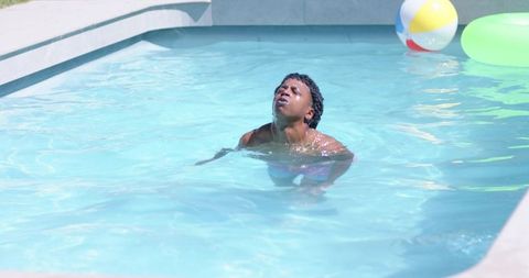 Young man treading water in sunlit backyard pool with inflatable beach ball and ring