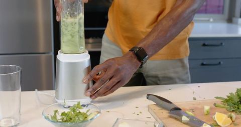 African American man preparing green smoothie in modern kitchen while wearing smartwatch