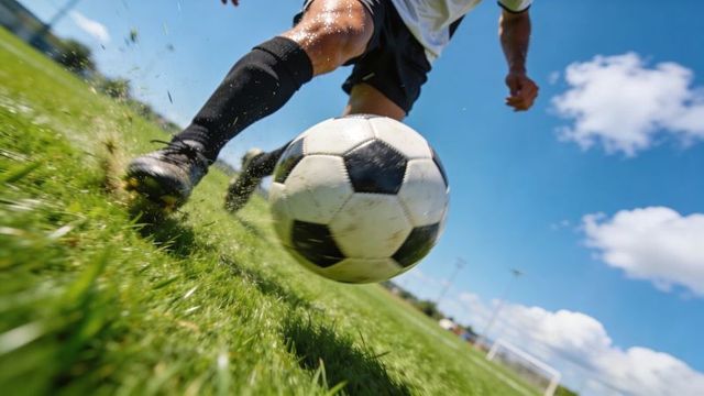 Dynamic low-angle closeup of soccer player kicking ball on grass, motion spray and cleats