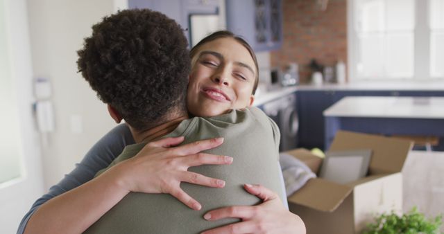 Couple happily embracing in their new home, surrounded by moving boxes. Ideal for use in content related to new beginnings, family life, real estate, home decor companies, and relationship advice.
