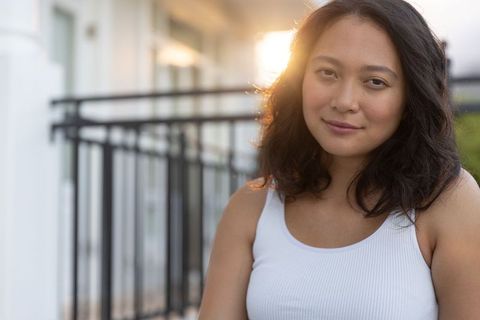 Asian woman relaxing on balcony at golden hour with warm backlight and sun flare