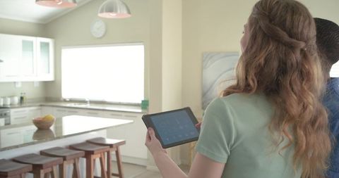 Diverse couple controlling smart home with tablet in bright modern kitchen with marble island