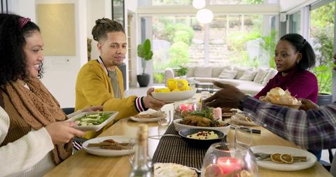 Diverse friends sharing cozy home dinner passing roast chicken corn and sides