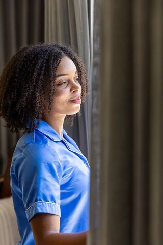 African american woman gazing out hotel window wearing blue collared shirt serene reflection