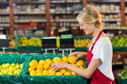Smiling female clerk organizing oranges in supermarket produce aisle
