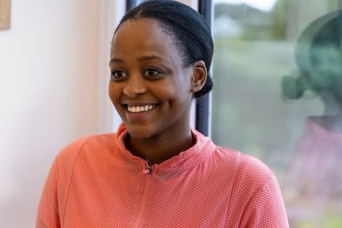Young african american woman smiling by window in pink zip-up with lavalier mic