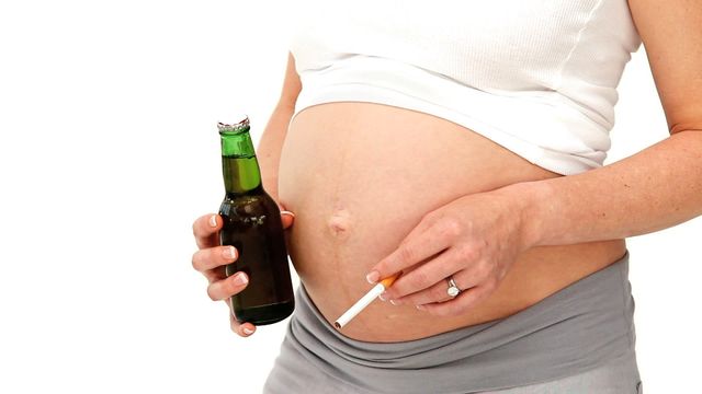 Pregnant woman shown holding cigarette and beer bottle against a plain white background. Related to risky health behaviors during pregnancy and maternal addiction. Useful for health education, awareness campaigns, or articles regarding prenatal care and risks of substance abuse.