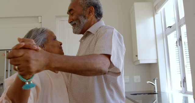 Side view of senior black couple dancing together in kitchen at comfortable home. They are smiling and holding hands 4k