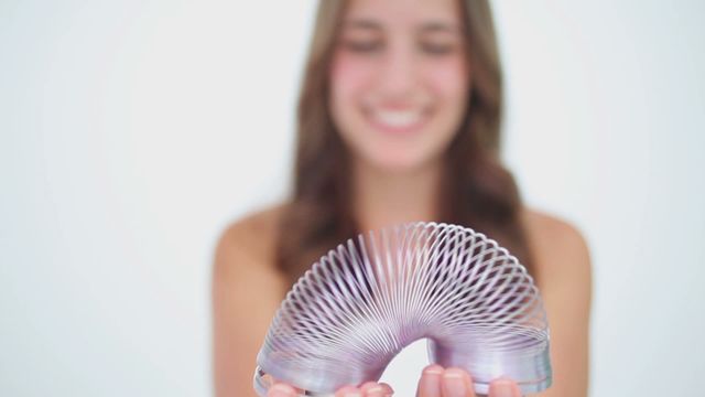 This image captures a cheerful woman focused on enjoying a plastic metallic slinky, conveying fun and nostalgia. Perfect for editorial uses portraying happiness or for designs evoking childhood memories. It can be used in advertisements targeting stress relief, entertainment products, or as a digital asset for articles and blogs about leisure and relaxation.