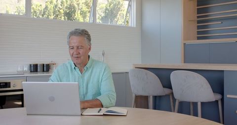 Senior Man in Modern Kitchen Working on Laptop Smiling