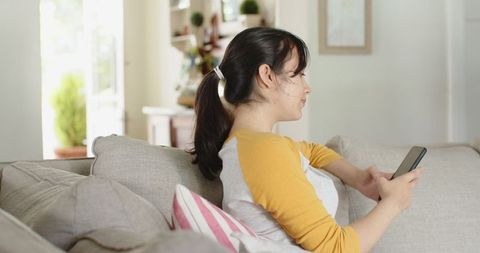 Young Woman Relaxing on Sofa Using Smartphone in Cozy Living Room