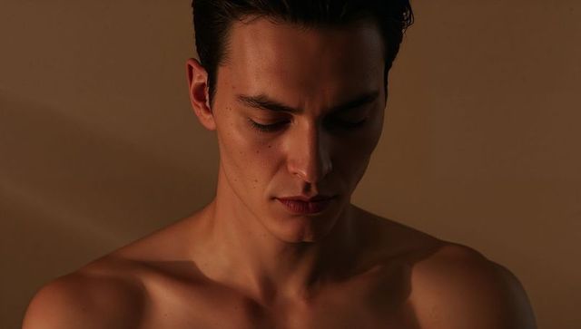 Young man lowering head contemplating in warm chiaroscuro side lighting, intimate closeup