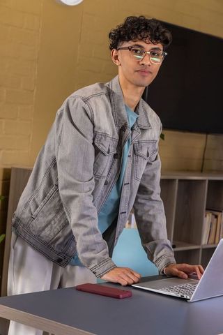 Asian young professional leaning at desk using laptop and smartphone in minimalist workspace