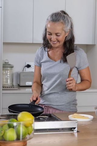 Middle-aged woman cooking on stovetop with nonstick pan and spatula in modern kitchen