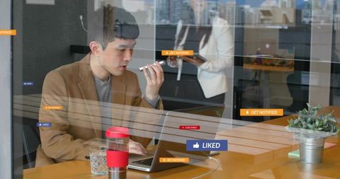 Chinese professional using laptop and smartphone with social notifications in glass office