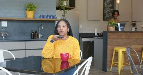 African american woman speaking into phone at modern cafe table with red mug