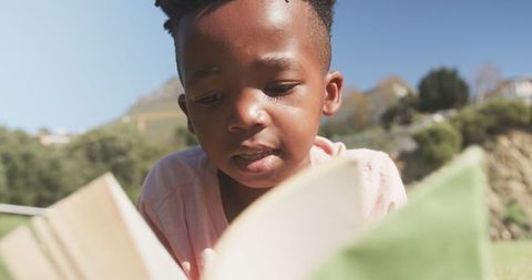 Young Boy Engaged in Reading Outdoors on Sunny Day