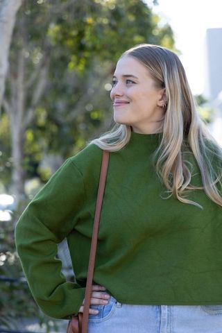 Young woman wearing green sweater and denim jeans, carrying brown bag, looking right