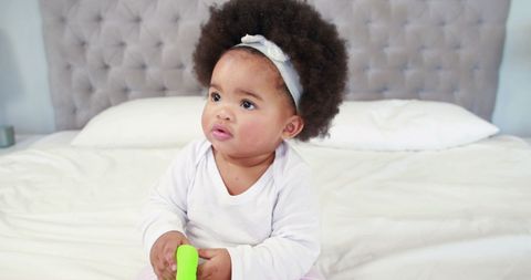 Adorable Baby Sitting on Bed with Curly Hair