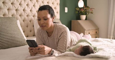 Mother Relaxed with Baby on Bed Using Smartphone Home Comfort