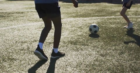 Diverse teenagers kicking and controlling soccer ball on sunlit artificial turf during practice