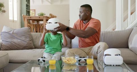 African American Father Placing VR Headset on Son on Couch for Family Gaming Bonding
