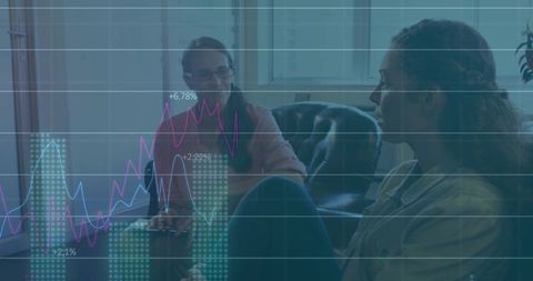 Two women collaborating on financial data tablet with graph overlay in office lounge
