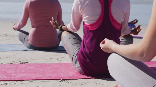 Women are enjoying a peaceful yoga meditation session on the beach on a sunny day. They are all sitting in a row on yoga mats and practicing mindfulness together. Ideal for promoting wellness, relaxation, mindfulness, fitness routines, and wellness retreats. Suitable for websites and promotional materials related to fitness, meditation, yoga classes, and health resorts.