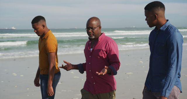 Father and two sons walking on beach, engaged in conversation. Expressions indicate meaningful discussion and bonding. Ocean waves in background, casual clothes, sunny day. Perfect for family, relationship, and outdoor activity concepts. Ideal for websites, advertisements, or articles focusing on family time, counseling, fatherhood, and nature.
