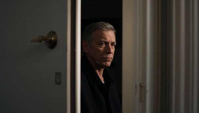 Senior man standing in dim doorway moody portrait with brass door handle, drapery, muted lighting