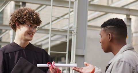 Diverse graduates exchanging diploma under glass canopy on modern campus architecture
