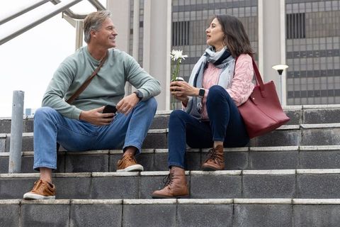 Middle-aged couple sitting on city steps holding daisies and smiling during conversation