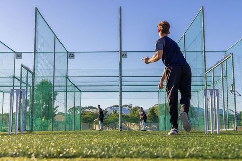 Right-arm bowler delivering ball in cricket nets with batsmen practicing outdoor training