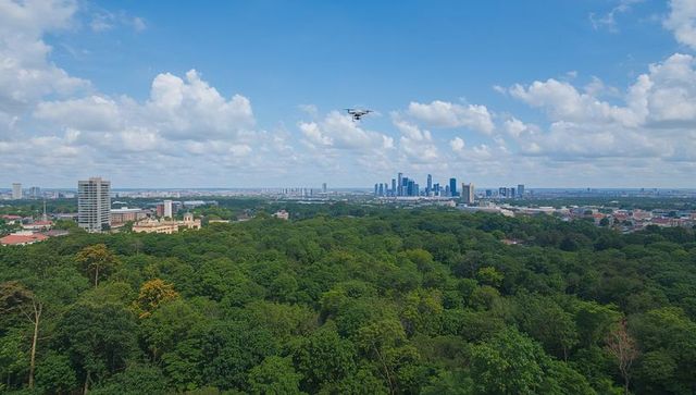 Aerial drone hovering over lush urban forest with distant modern city skyline panorama