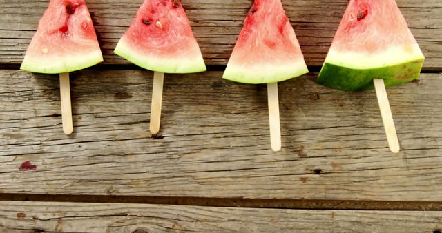 Slices of watermelon on popsicle sticks are arranged on a rustic wooden background, with copy space. These refreshing watermelon popsicles offer a creative and healthy treat option for hot summer days.
