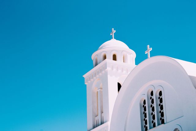 White Greek Orthodox Church with distinctive dome and crosses standing prominently under a clear blue sky. Could be used for travel brochures, websites on Greek tourism, religious studies materials, inspirational posters highlighting beauty and spirituality.