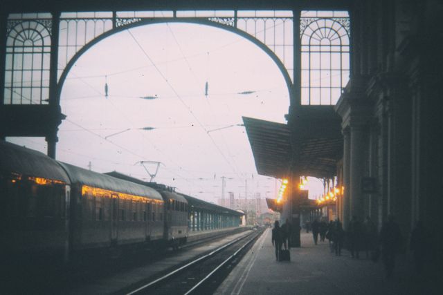 Old train on platform showcasing early morning travel atmosphere with silhouette of people walking along platform. Well-suited for projects related to travel, history, transportation, and architecture.