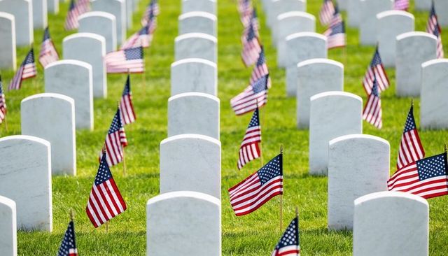 Rows of marble headstones with american flags honoring fallen veterans in sunlit cemetery