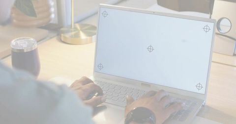 Man typing on silver laptop at minimalist wooden desk wearing wristwatch and daylight lamp