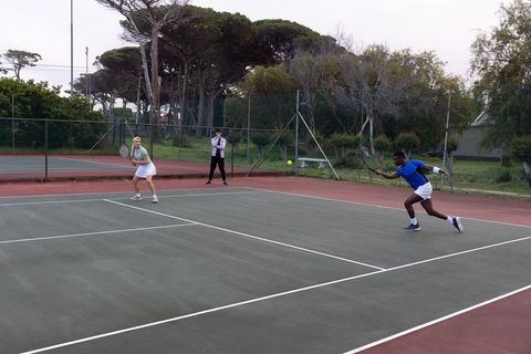 Diverse mixed doubles team lunging for volley on outdoor hardcourt while coach observes
