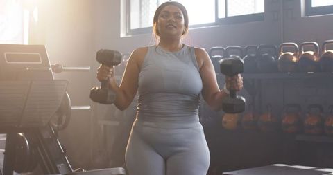 Mid-adult african american woman lifting dumbbells in sunlit gym building strength