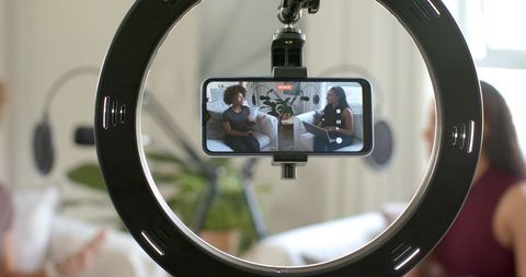 Recording podcast with smartphone in ring light showing two women cohosts on couch