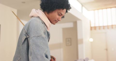 Contemplative african american man leaning in denim jacket and pink hoodie at home