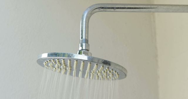 Close-up view of a water stream flowing from a modern showerhead in a bathroom. Ideal for promoting home improvement, plumbing services, cleaning products, or bathroom lifestyle themes. Image emphasizes cleanliness, modern design, and refreshing elements.
