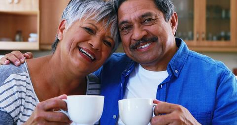 Senior Couple Enjoying a Warm Drink in Cozy Kitchen with Smiling Faces