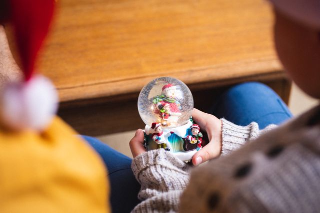 Rear view of boy holding a snow globe while sitting at home during christmas. christmas festivity and celebration concept