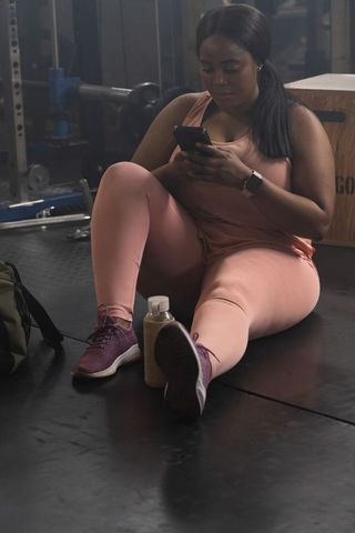 African american woman resting and scrolling smartphone after workout in gym